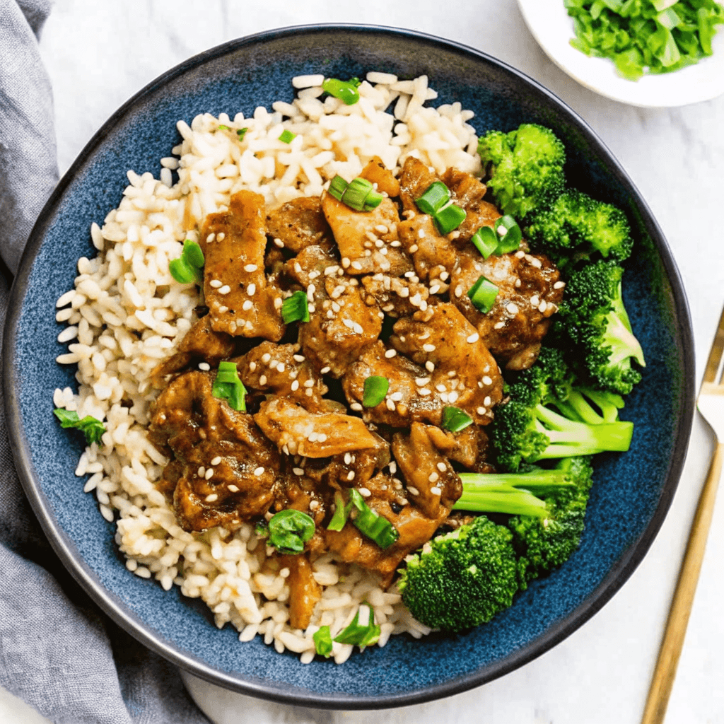 ultra-close-up, high-quality image of a single slow cooker honey garlic chicken serving, capturing its glossy, sticky glaze, tender shredded texture, and deep golden-brown color with intense focus. The dish should be placed in a shallow white bowl, with a soft blur in the background. Bright natural light highlights the glistening sauce and juicy chicken pieces. Garnished with finely chopped green onions and sesame seeds. No other elements are visible.