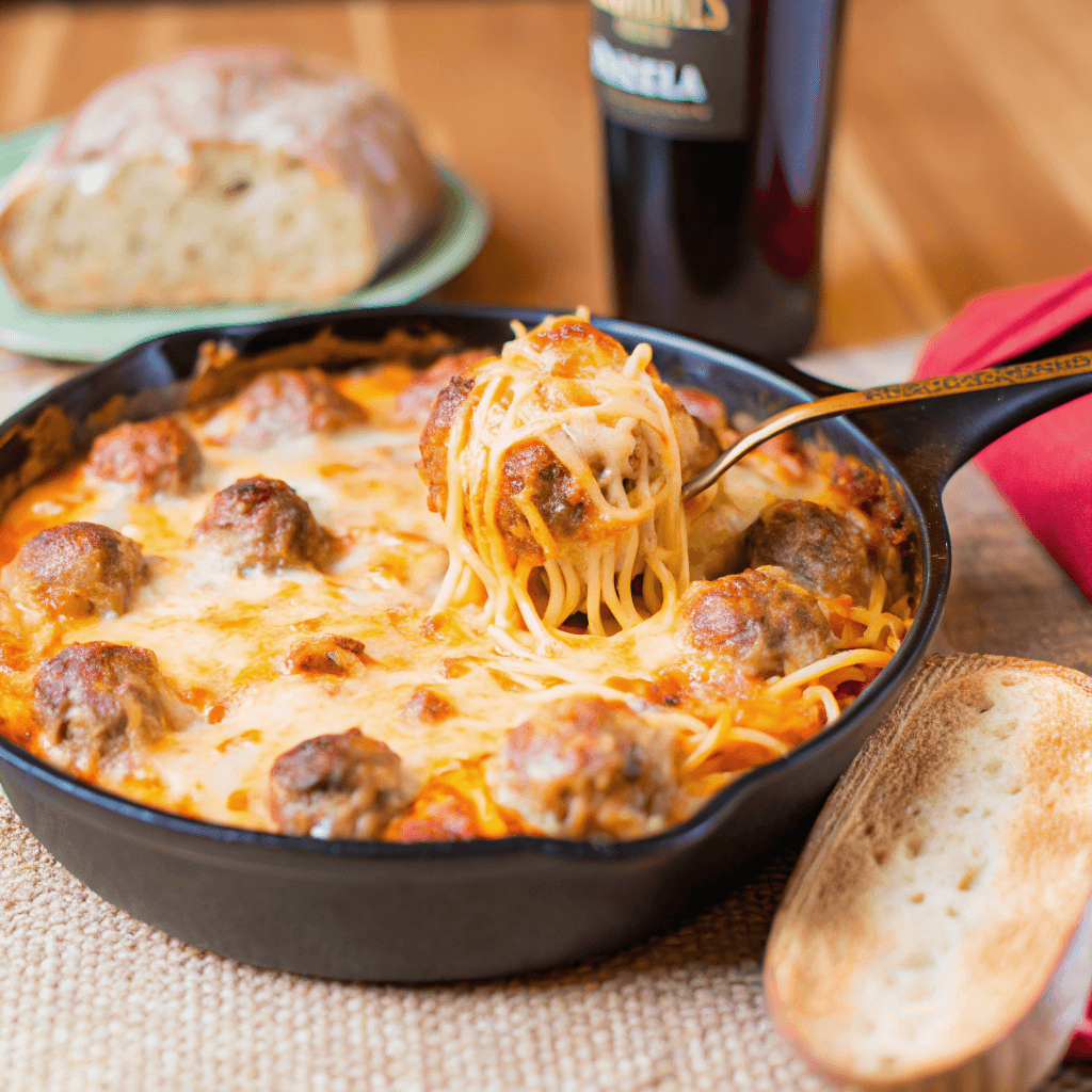 ultra-close-up, high-quality image of a single serving of baked spaghetti and turkey meatballs, capturing the bubbling melted cheese, vibrant red marinara, and golden edges. The dish is nestled in a white ceramic bowl, with stringy mozzarella stretching from fork to pasta. Background softly blurred to emphasize rich textures, with fresh basil leaves adding a pop of green.